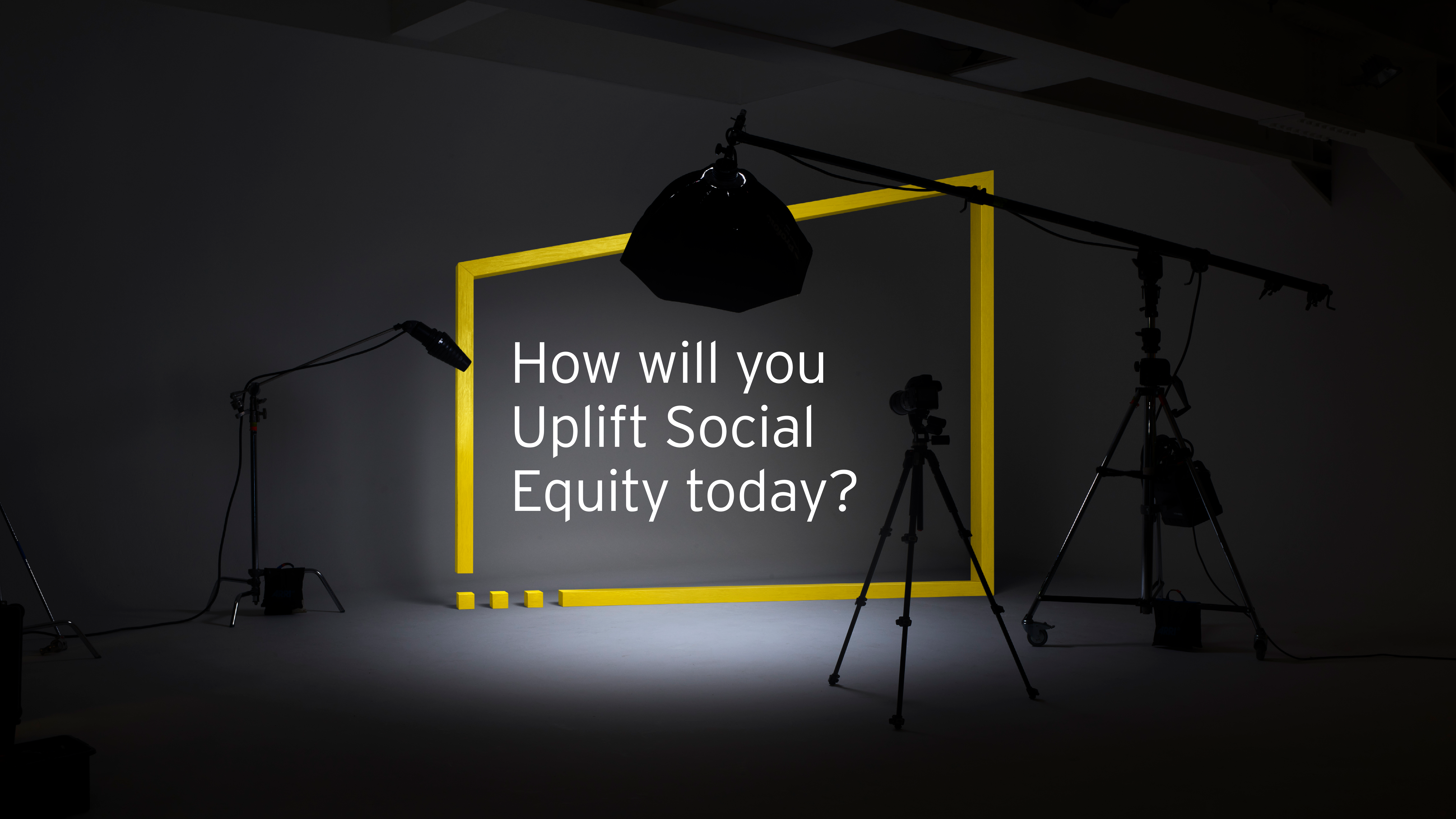 A yellow box sits on a photoset with lights pointing at it, text inside reads 'How will you Uplift Social Equity today?'
