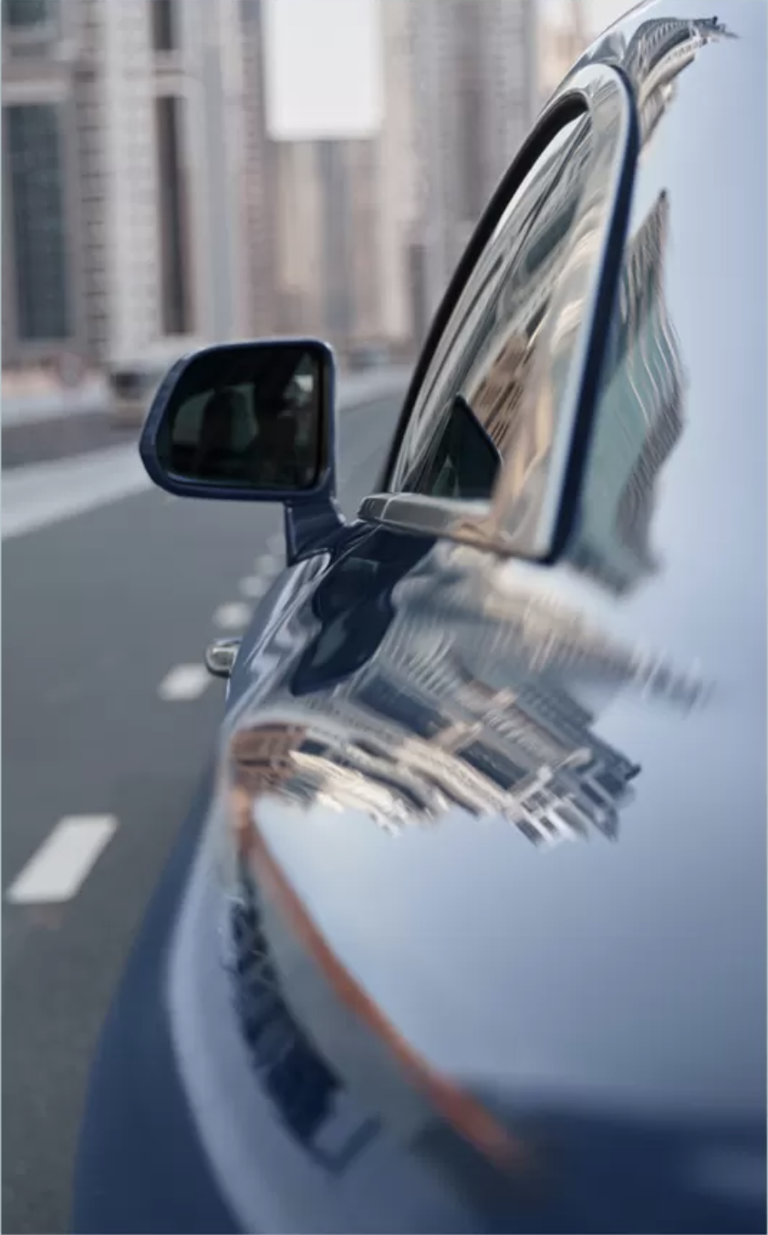 A 9:16 image of a blue rolls royce spectre with the reflections of a modern city in the paintwork near the camera